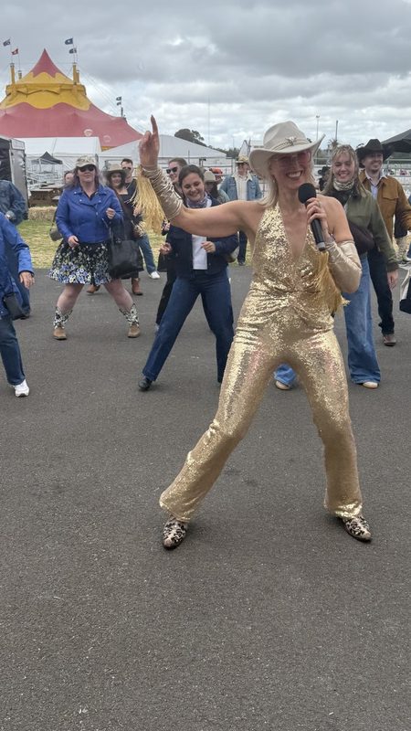 Kirsten Mann in a gold jumpsuit leading a festival crowd