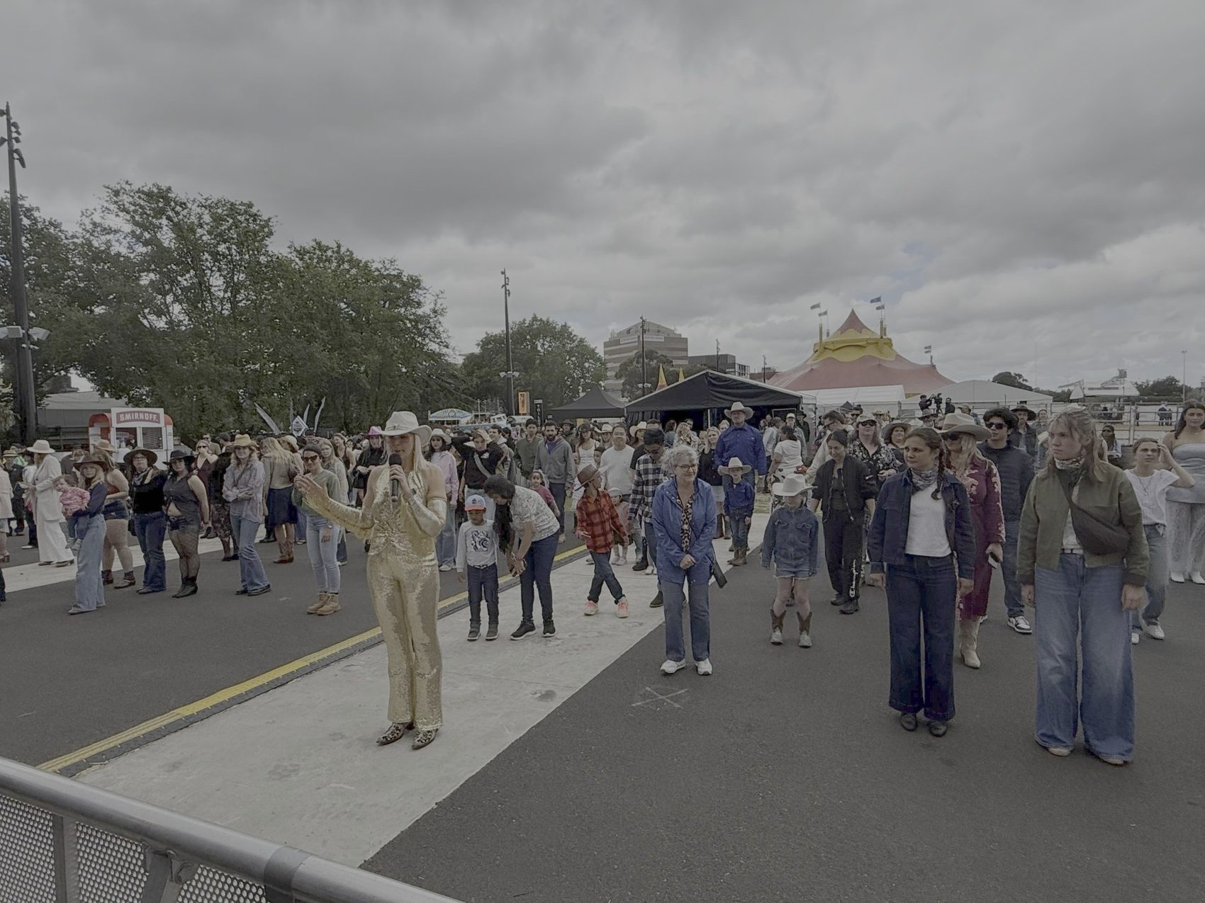 Kirsten Mann in a gold jumpsuit leading a big festival crowd in line dancing