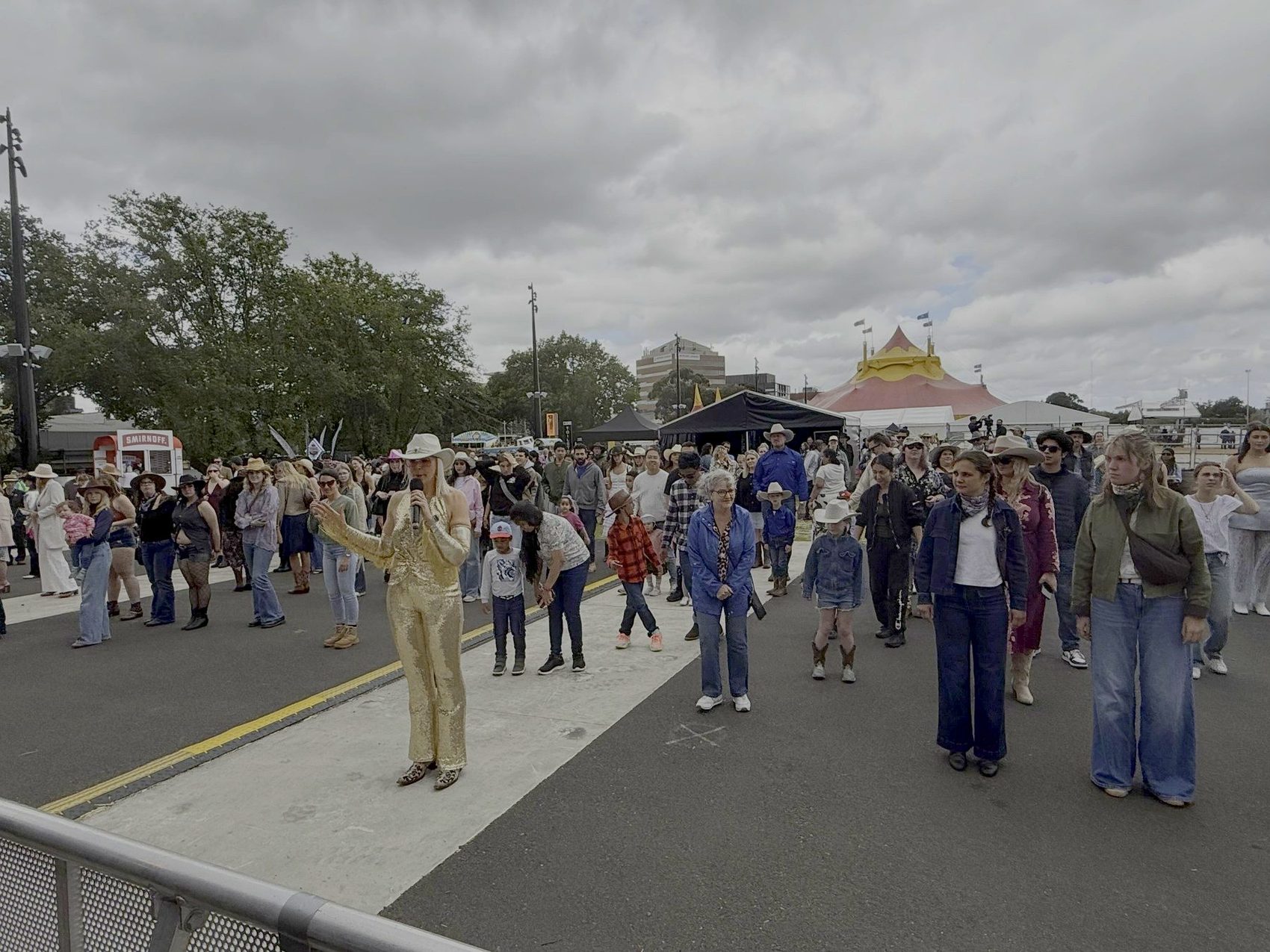 Kirsten Mann in a gold jumpsuit leading a big festival crowd in line dancing