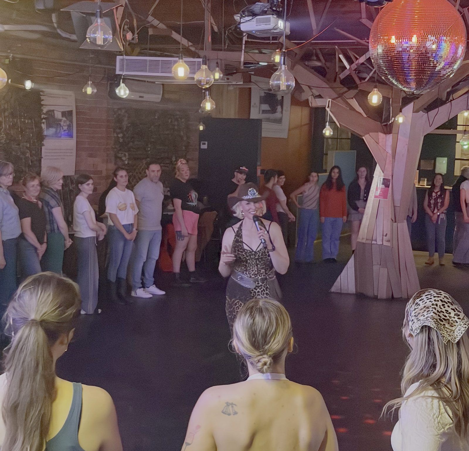 Kirsten Mann hosting a public line dancing event, teaching a whole room to dance under a disco ball