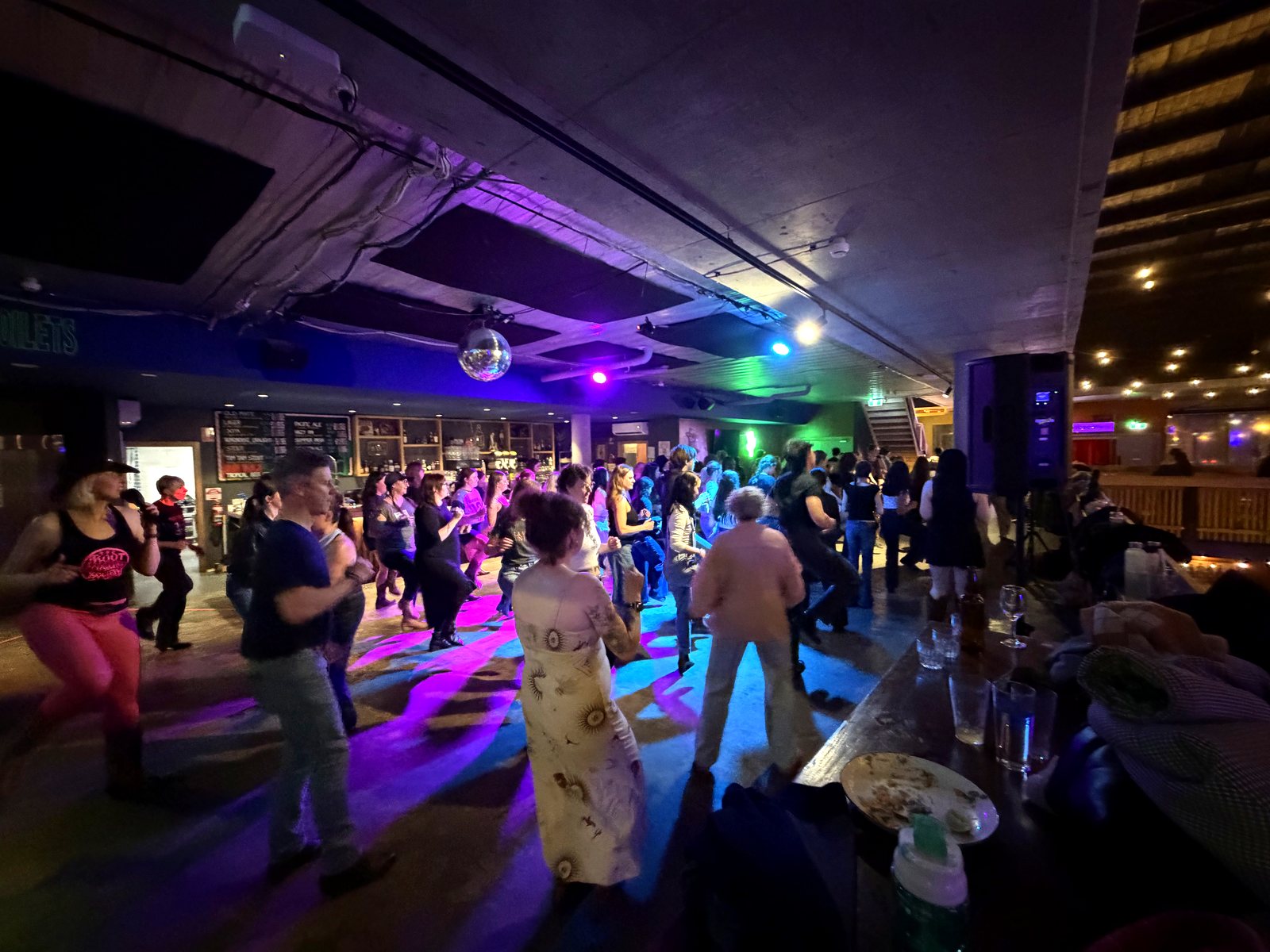 A packed Boot Scooting Society night — the crowd line dancing together under the disco ball