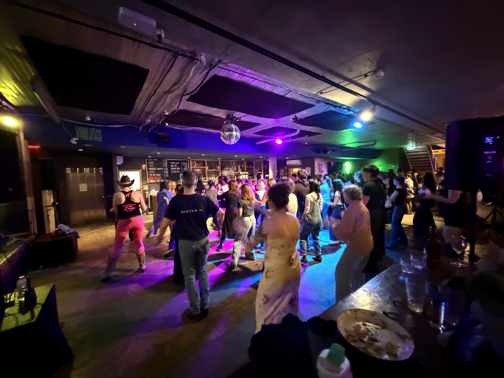 A packed Boot Scooting Society night — the crowd line dancing under the disco ball at the City of Melbourne Bowls Club